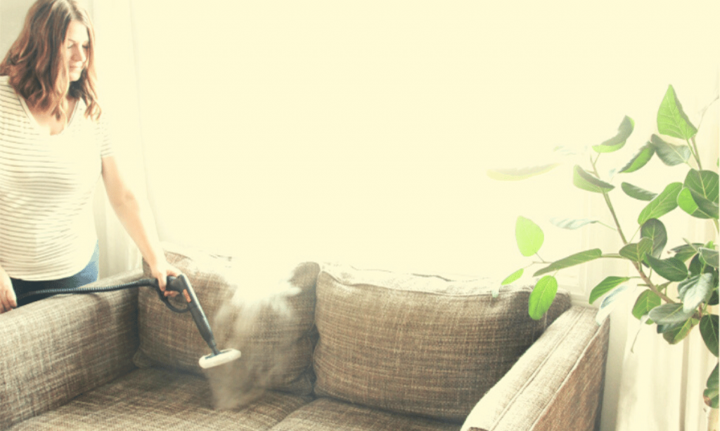A woman steam cleaning a couch.
