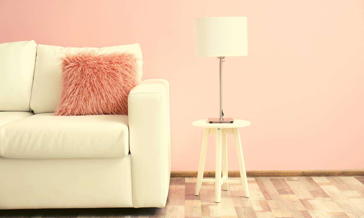 A white couch with a pink pillow on it and a white lamp next to it.