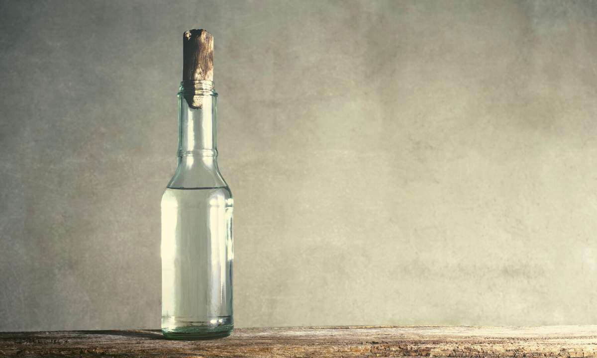 A glass bottle of vinegar on a wooden table with a gray wall in the background.