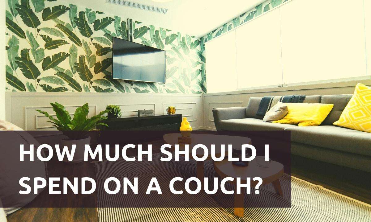 Living room with a gray couch and leaf-patterned wallpaper. Text reads: "How Much Should I Spend On A Couch?"