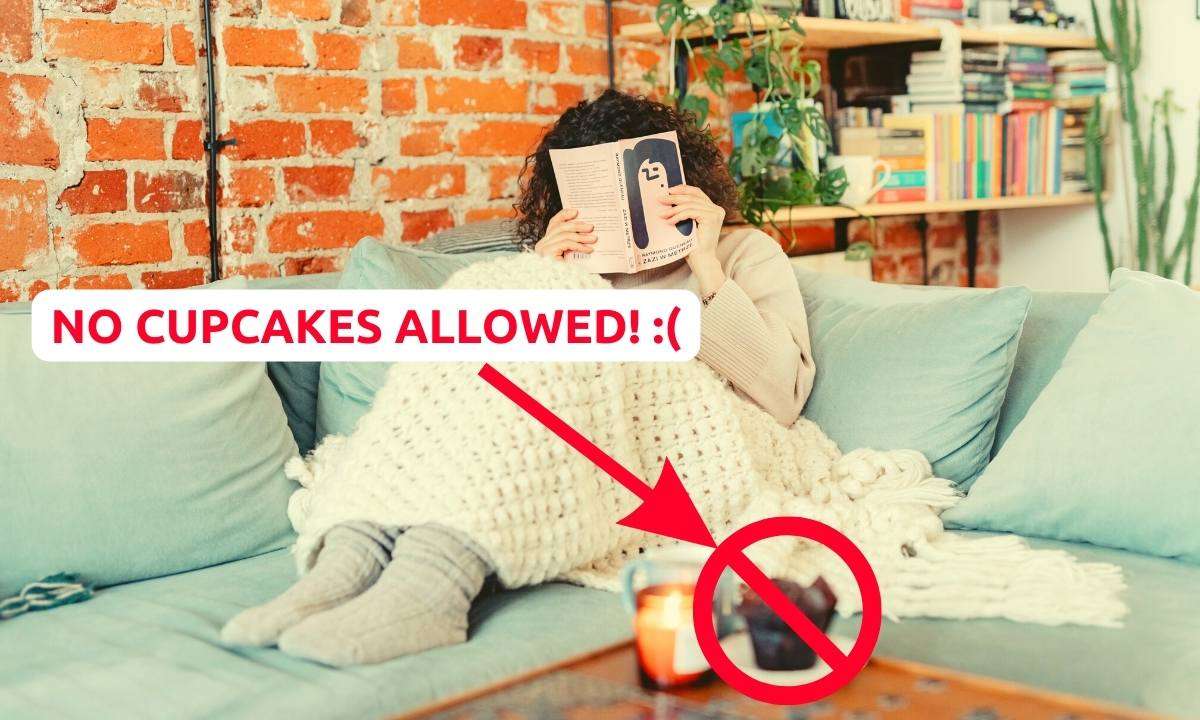 A woman sitting on a blue sofa holding a book in front of her face. On the coffee table is a cupcake. Next to it are the words: "No cupcakes allowed! :("