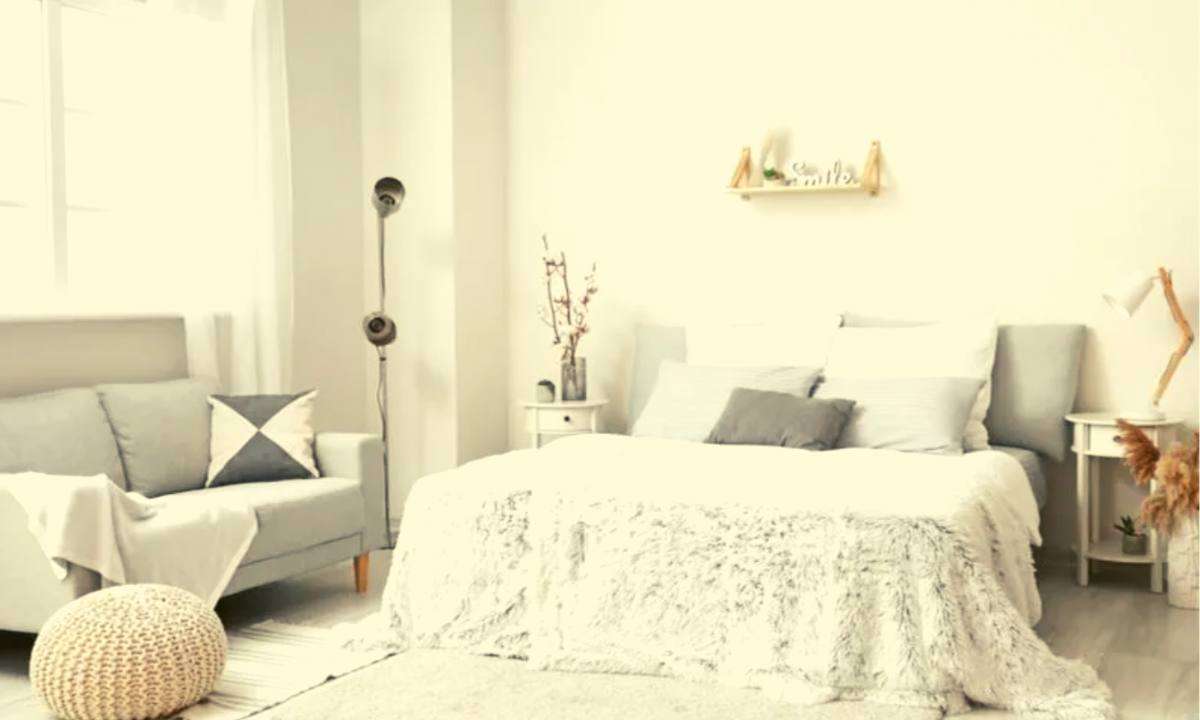 A gray love seat near a white bed.