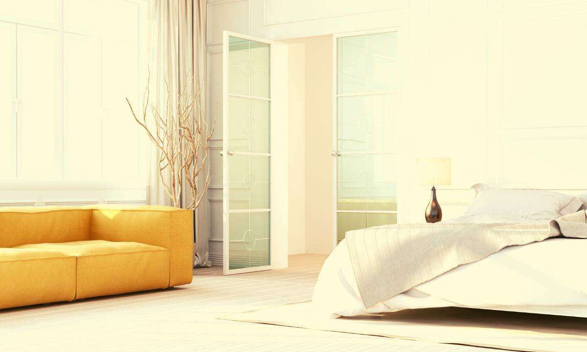 A sunny bedroom with a yellow couch against a window.