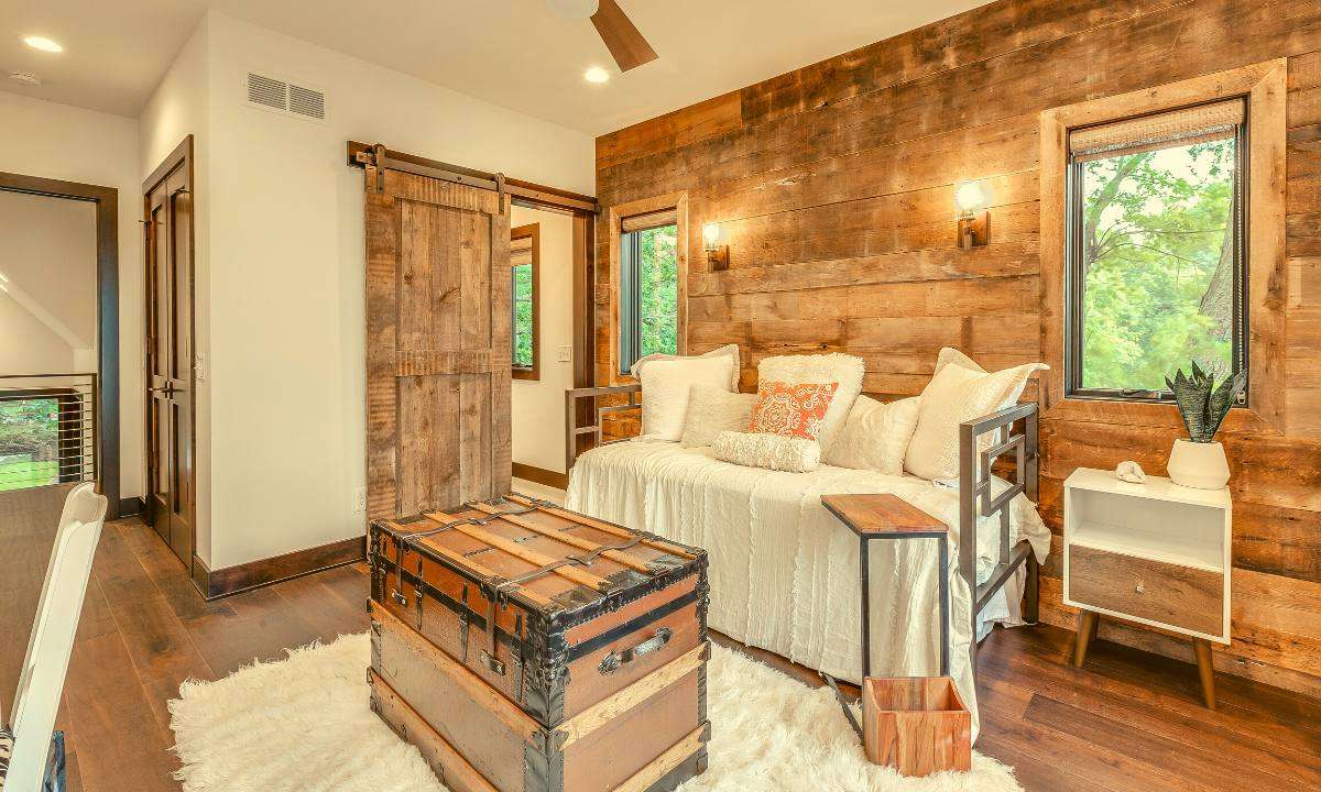 A daybed with a white blanket and pillows sitting against a rustic wooden wall.