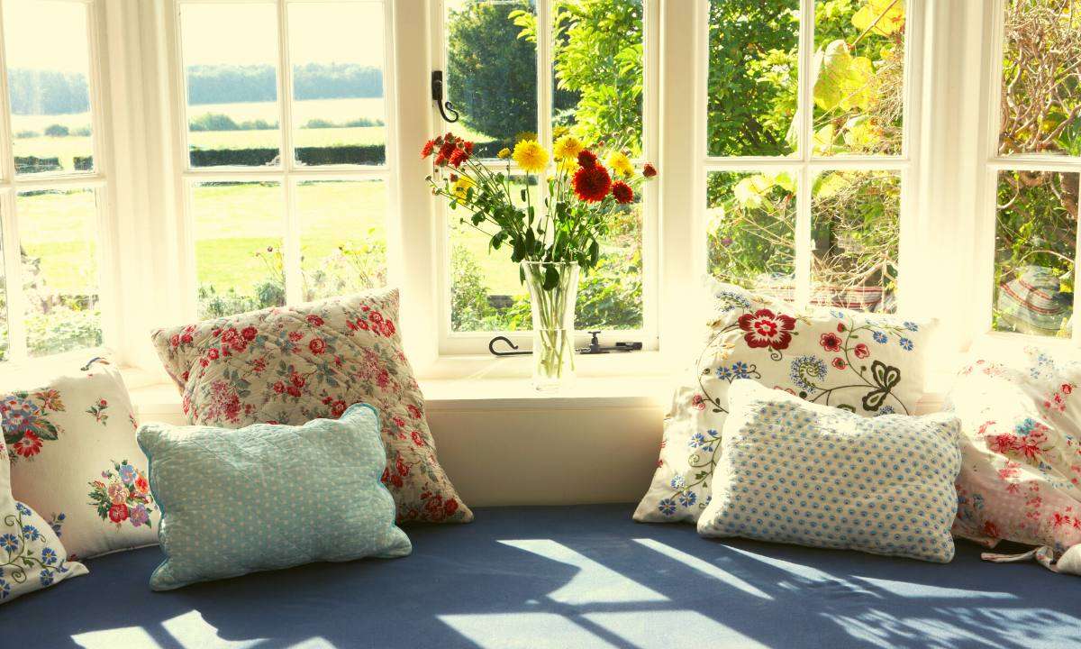 A sunny window seat with a blue cushion and floral-patterned pillows.