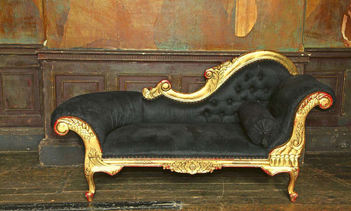 A black-and-gold chaise lounge against antique wood paneling.